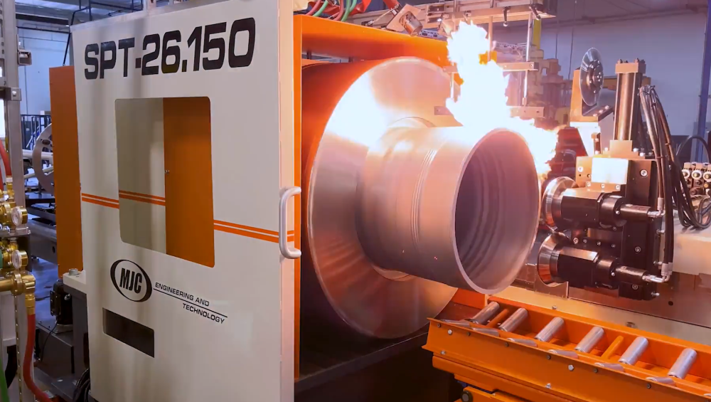 An industrial machine labeled 'SPT-26.150' by MJC Engineering and Technology performing a flame-hardening or heat-treating process on a large rotating metal cylinder, with visible flames along the workpiece surface.