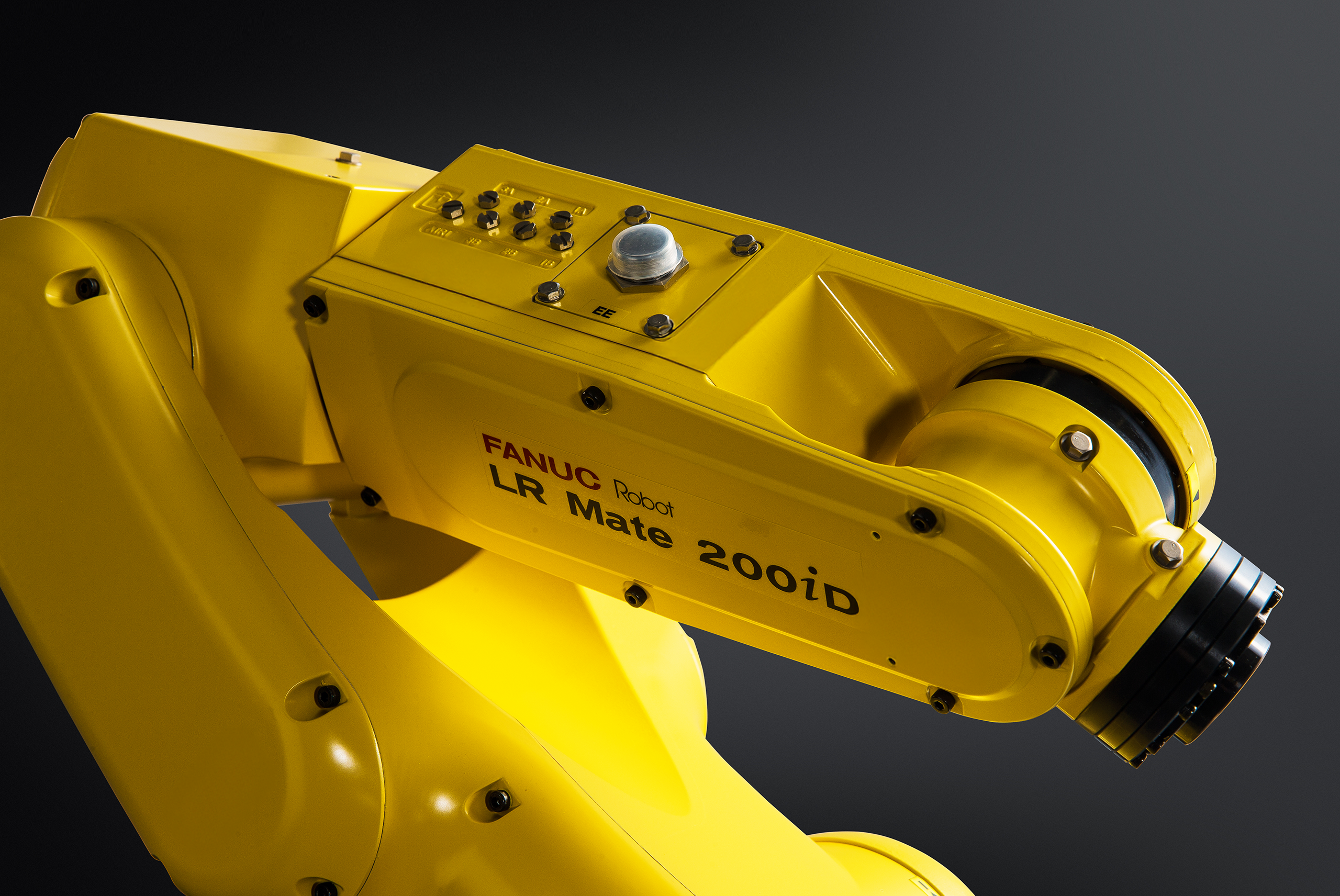 Close-up of a yellow FANUC LR Mate 200iD industrial robot arm against a dark background, showing its jointed forearm and wrist assembly with a black tool flange.