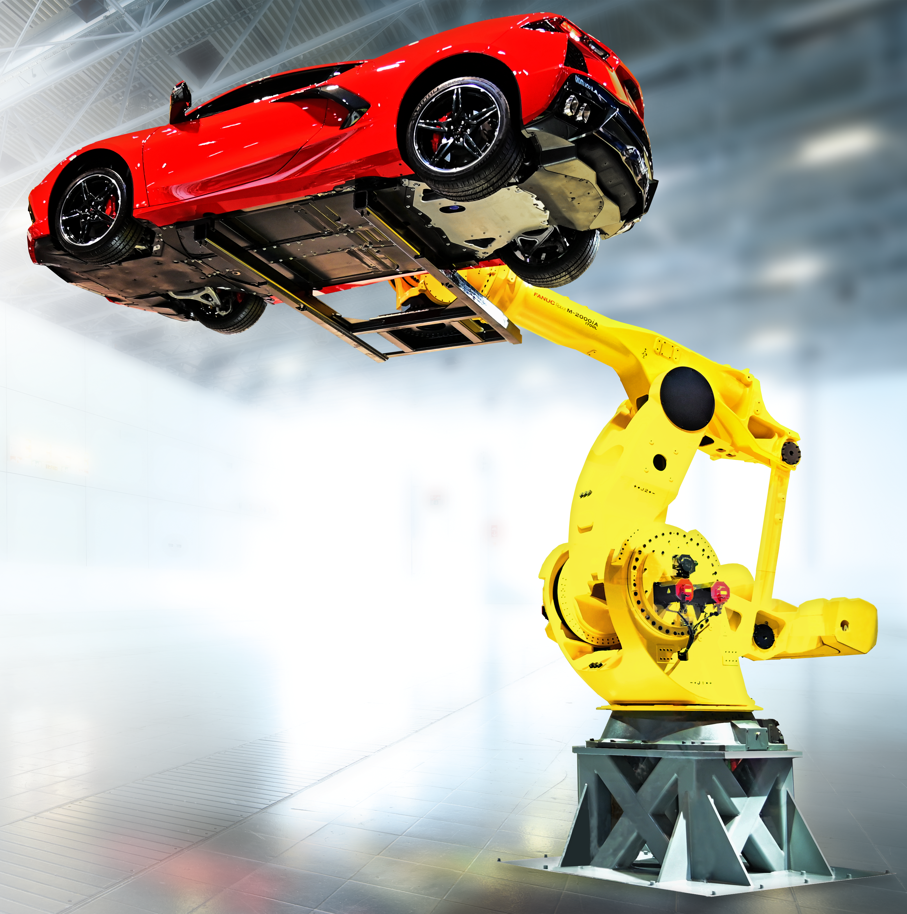 A heavy-duty yellow FANUC M-2000 industrial robot arm on a metal base, demonstrating its lifting capability by holding a red sports car aloft in a bright showroom setting.